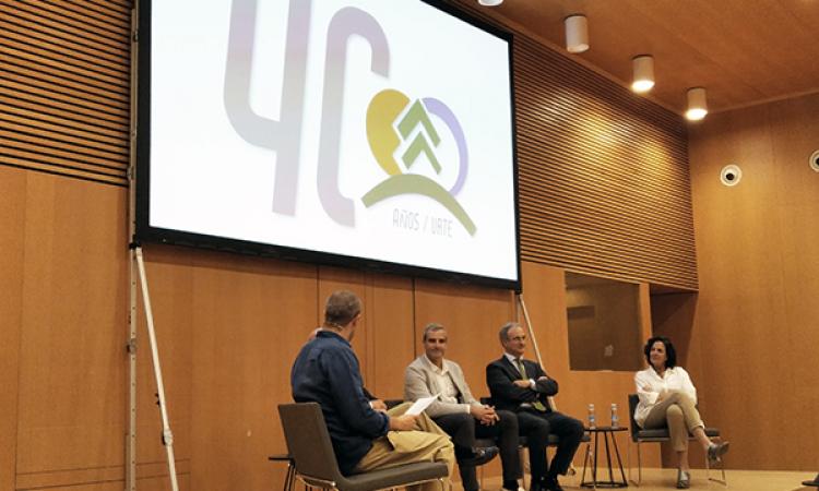 Imagen de la mesa coloquio de la Jornada. En la imagen, los participantes charlan con el moderador. Sobre ellos se proyecta una imagen del logotipo de 40 aniversario